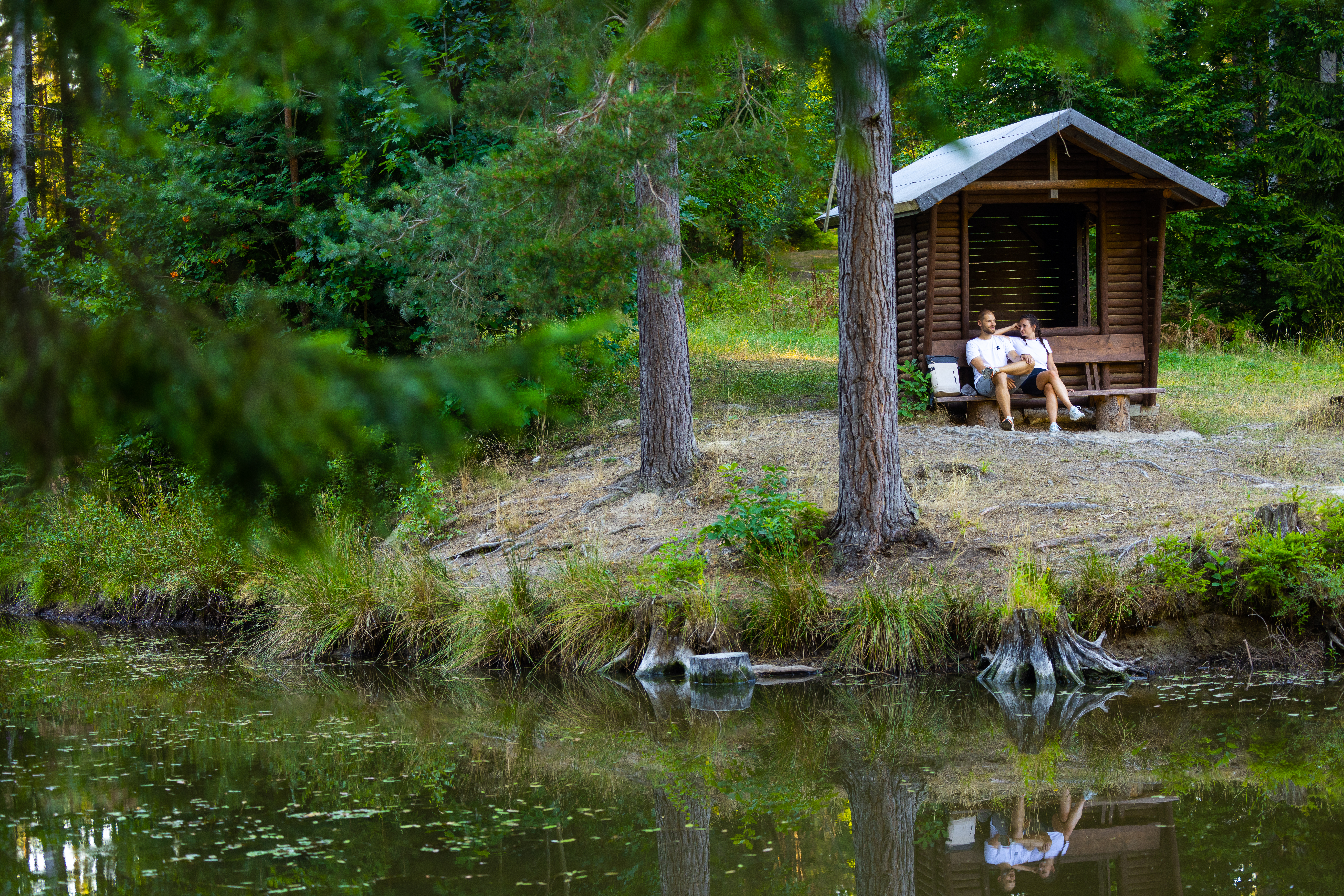 Ein Paar sitzt auf einer Bank vor einer Schutzhütte und genießt den Ausblick auf den Teich.